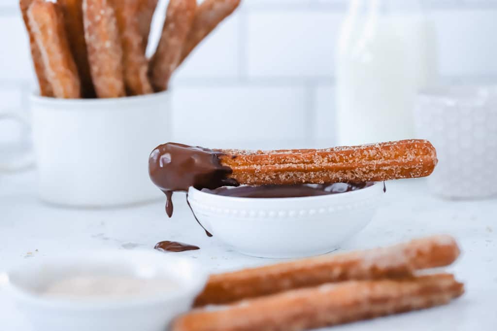 A single churro with chocolate sauce resting on a small bowl with chocolate dipping off