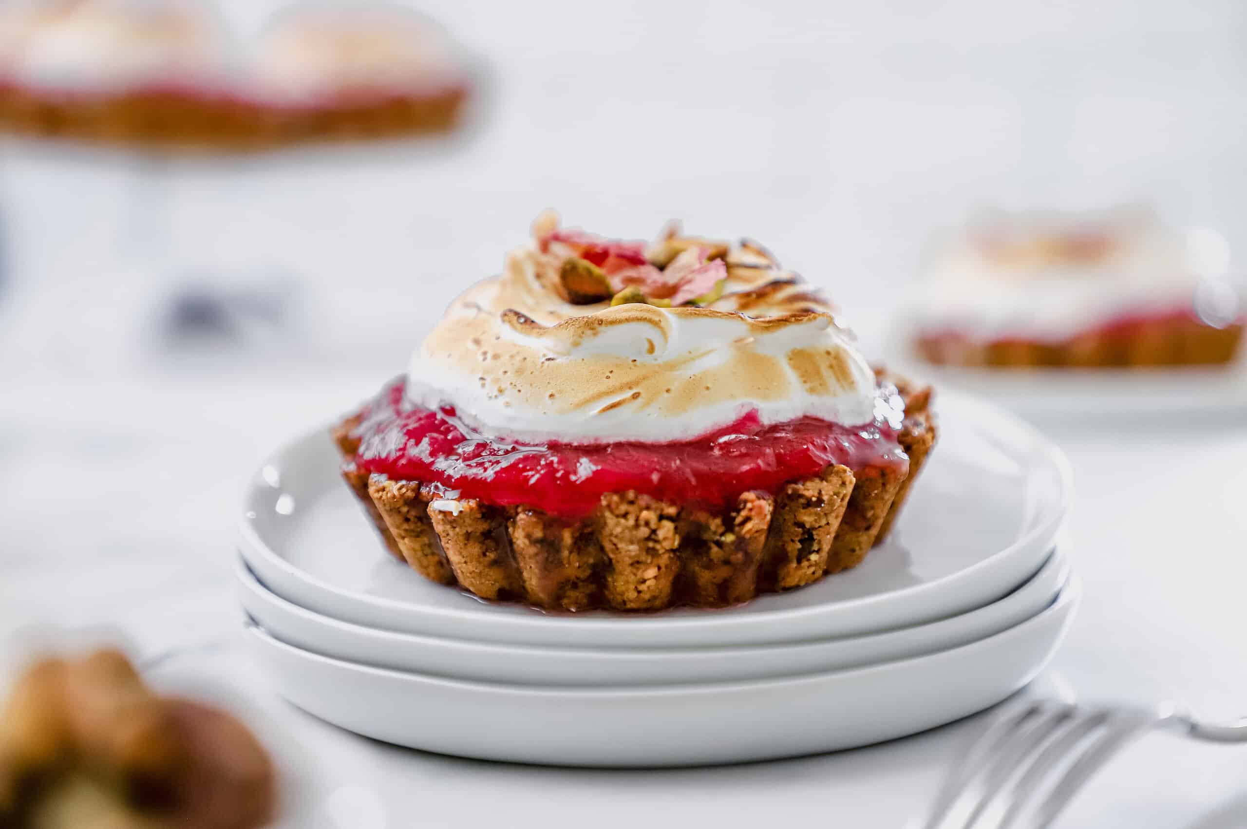 A close up shot of one of the pistachio rhubarb tarts on a stack of small white plates