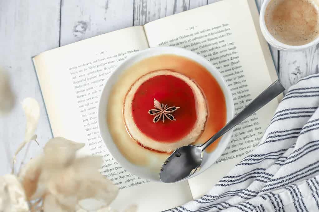 Looking down at a plate of pumpkin creme caramel on an open book with a shot of espresso